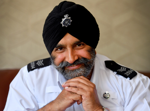 A Sikh policeman smiles while wearing a black turban and a white shirt