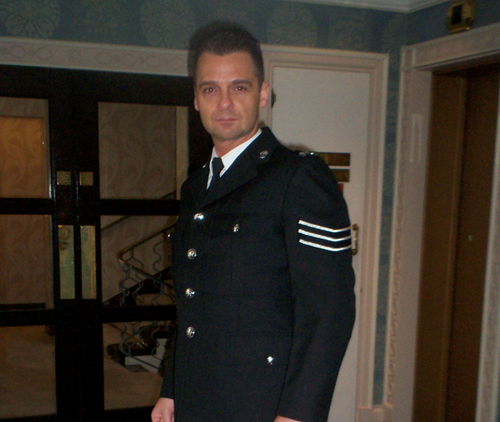 A middle-aged male police officer wears his uniform with buttons done up