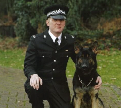 A policeman crouches down next to a kneeling police dog